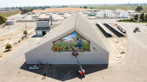 Aerial view of a large building with a mural of a field scene; a cherry picker is in use.