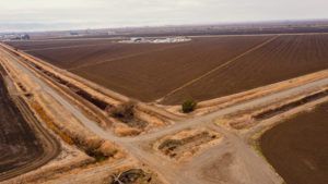 Aerial view of dirt roads intersecting near agricultural fields under a cloudy sky.