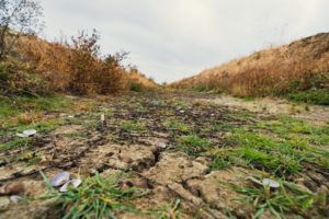 Dirt path flanked by hills with dry grass under a cloudy sky.