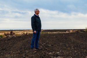 Man standing in a field, looking towards the horizon under a cloudy sky.