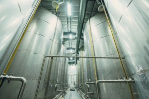 Stainless steel tanks in a factory setting, with pipes and ceiling lights.