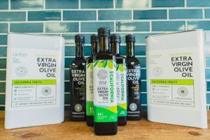 Olive oil bottles and containers on a wooden surface, in front of a blue tile wall.