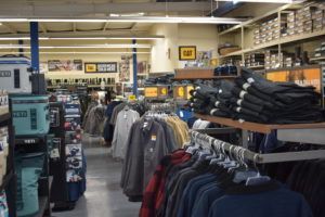 Clothing store interior with racks of jackets and pants, shelves with boots, and merchandise displays.