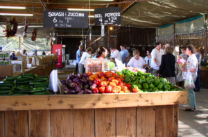 Produce stand with zucchini, bell peppers, and shoppers at an outdoor market.
