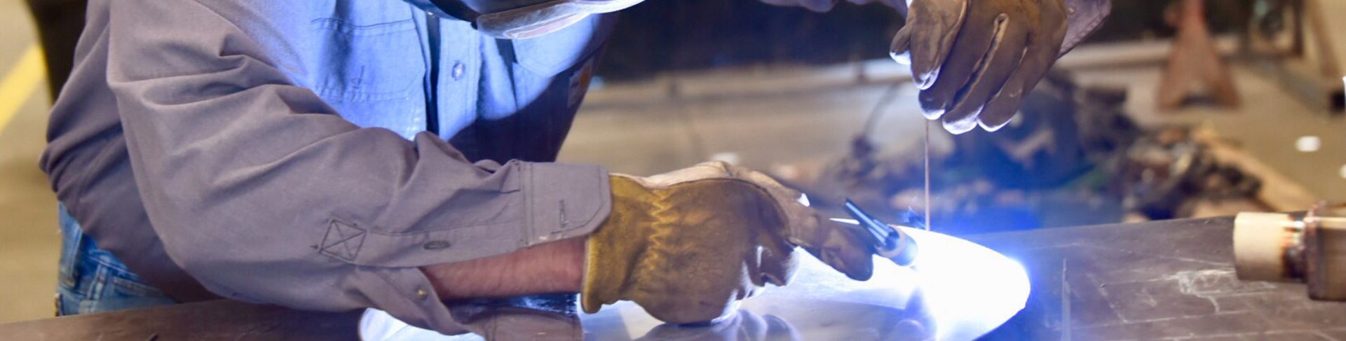 Person welding metal with protective gloves, bright blue sparks and light.