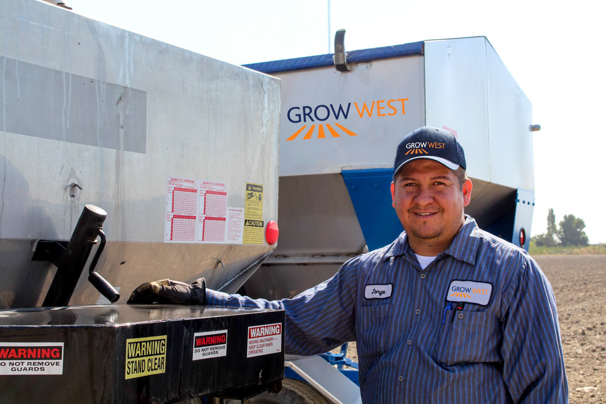 Man in a Grow West cap smiles beside farm equipment in a field; light blue and gray colors are visible.