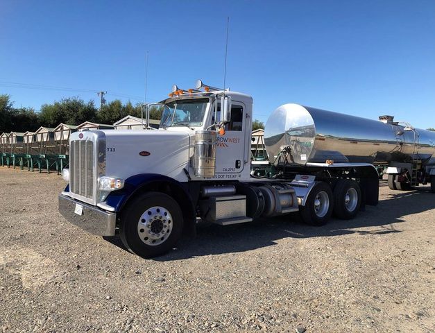 Silver and white tanker truck parked on gravel under a blue sky.