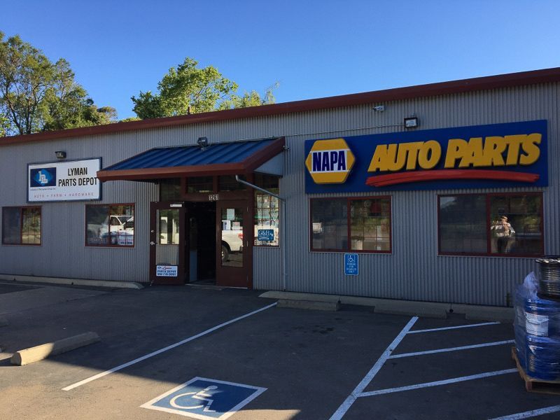 Exterior of a NAPA Auto Parts store with blue and yellow signage, a handicap parking space, and a customer in the window.