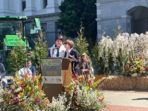 Two people speaking at a podium decorated with flowers; 