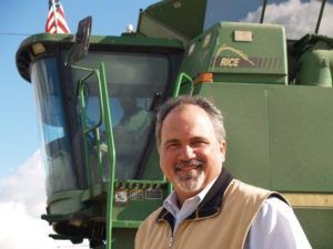 Man smiling in front of a green combine harvester; US flag on top.