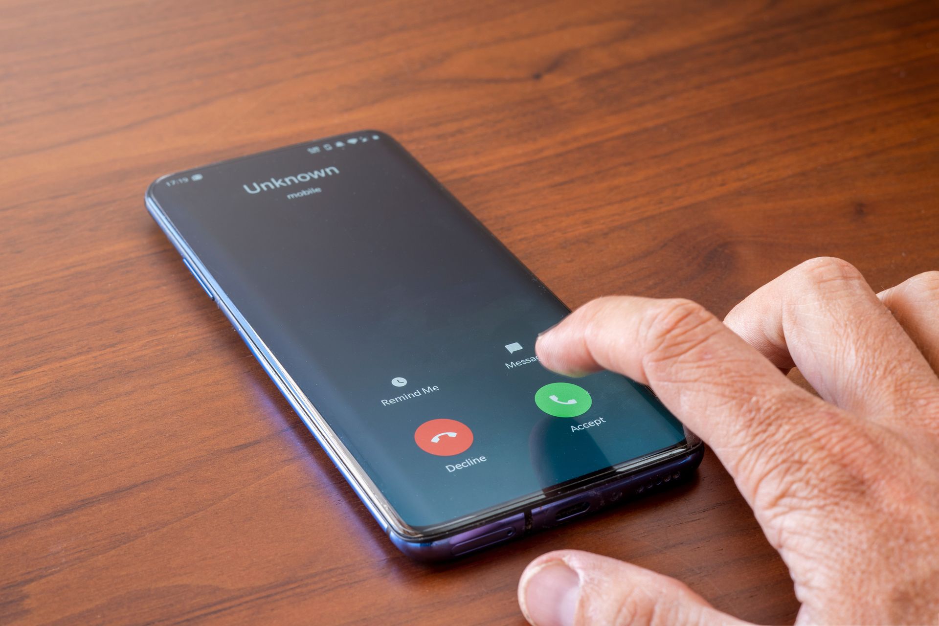 Hand tapping a smartphone screen showing an incoming call on a wooden table