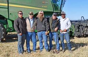 Five men pose in front of a green combine harvester on a harvested field, smiling.