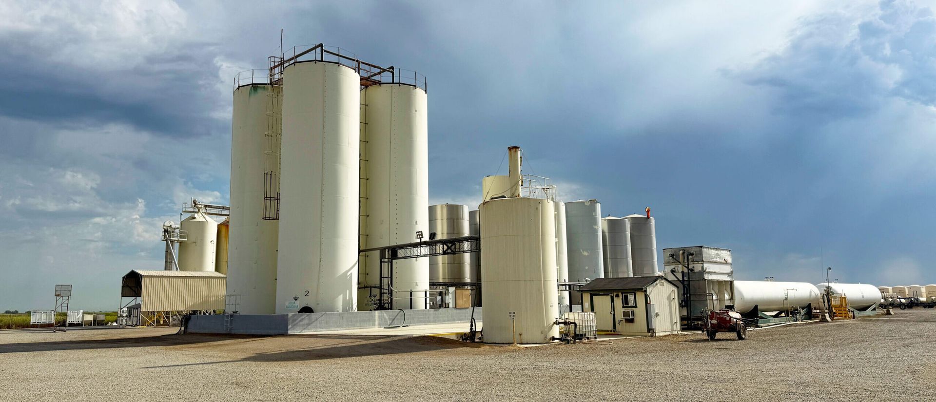 Oil and gas storage tanks in a barren landscape under a cloudy sky.