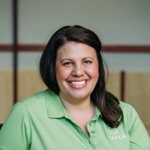 Woman with dark hair smiles, wearing a green polo shirt with 