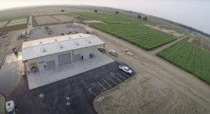 Warehouse building surrounded by agricultural fields; cars parked nearby.