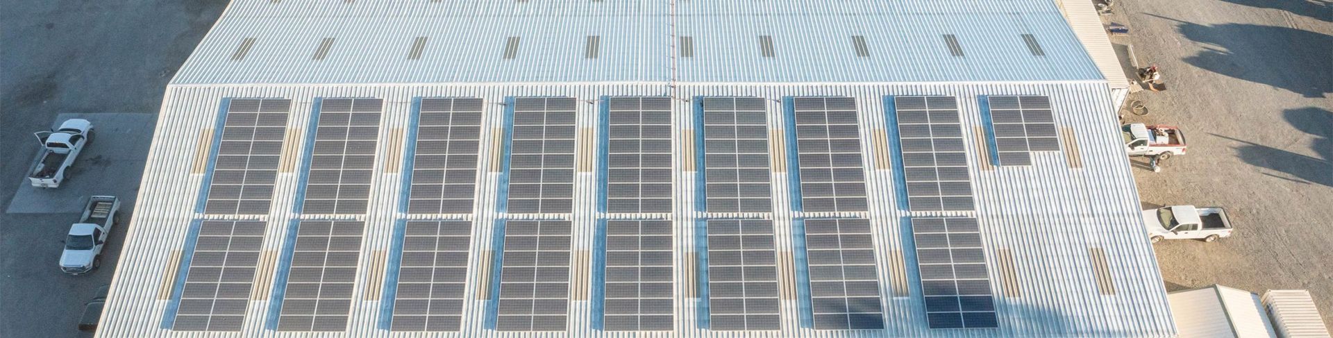 Aerial view of a building roof covered with solar panels. Two trucks are parked on the side.