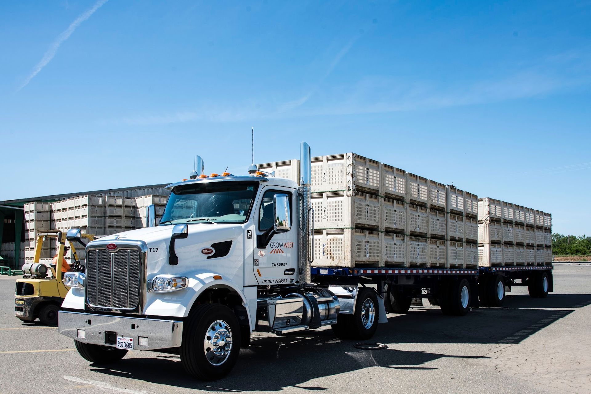 White semi-truck loaded with crates parked outside a building on a sunny day.