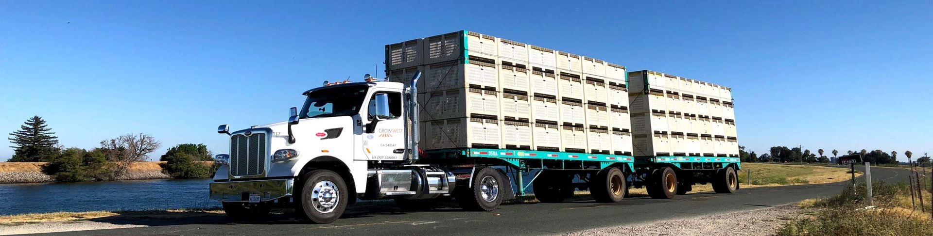 White semi-truck hauling stacked crates on a road under a blue sky.
