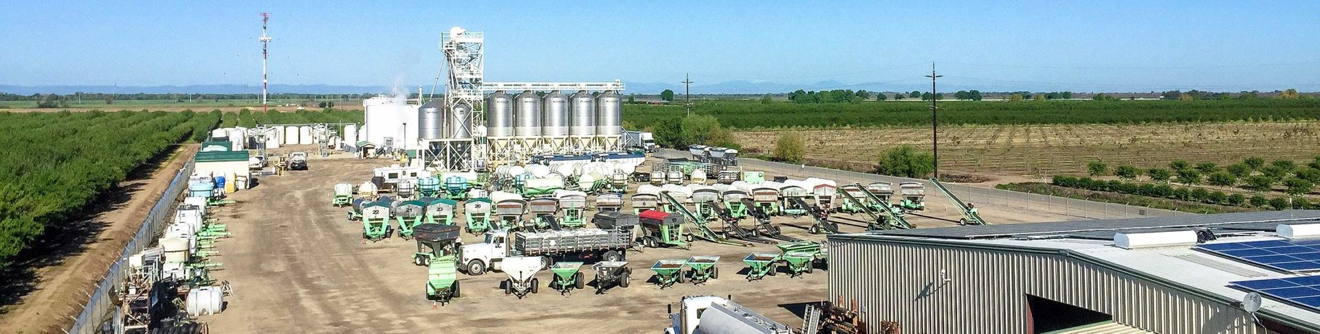 Aerial view of a farm processing plant with silos, machinery, and crops. Blue sky background.