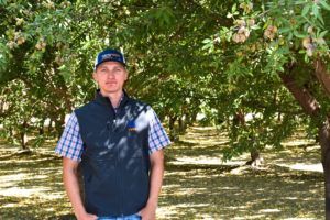 Man in vest and cap in orchard.
