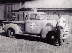 Man stands beside a vintage pickup truck, truck has Lyman Plumbing logo.