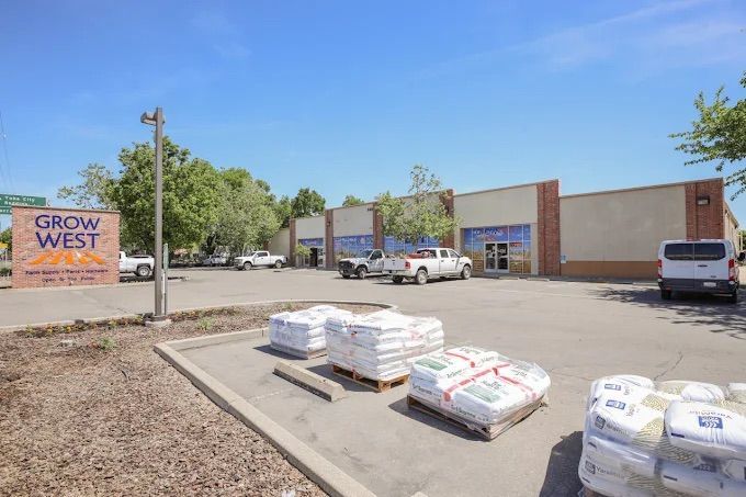 Grow West store with parked trucks, bags of products in front, sunny day.