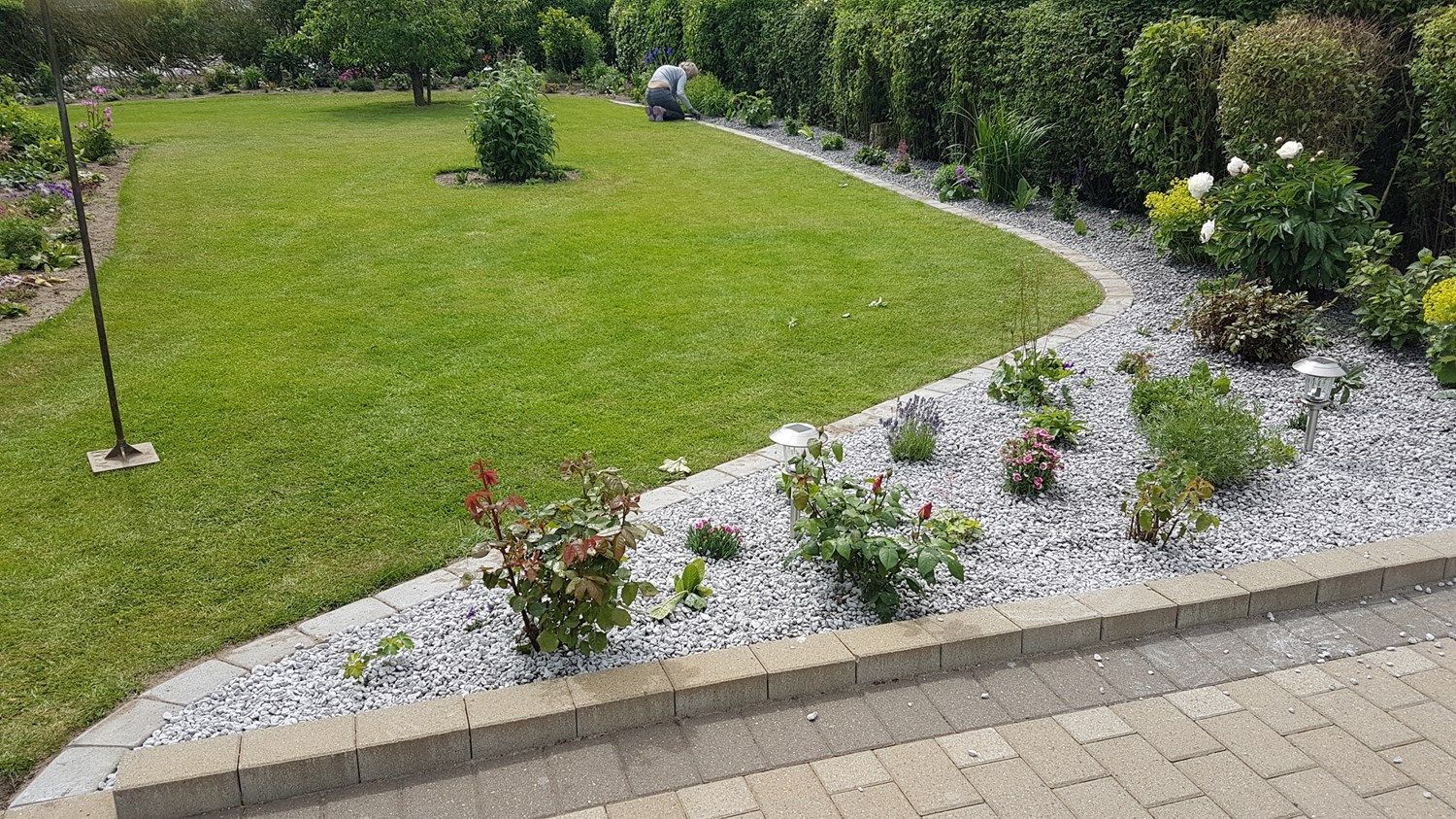 En frodig grøn græsplæne er omgivet af sten og blomster.