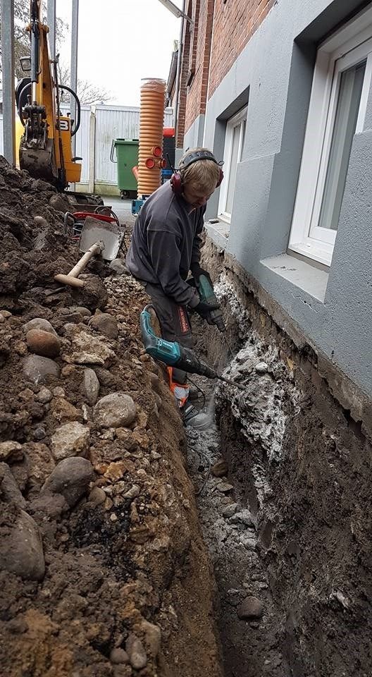 En mand graver et hul i jorden ved siden af en bygning.