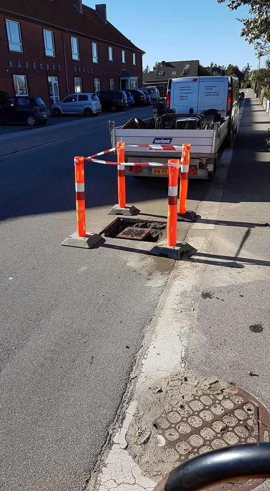 En lastbil holder parkeret i siden af vejen ved siden af et brønddæksel