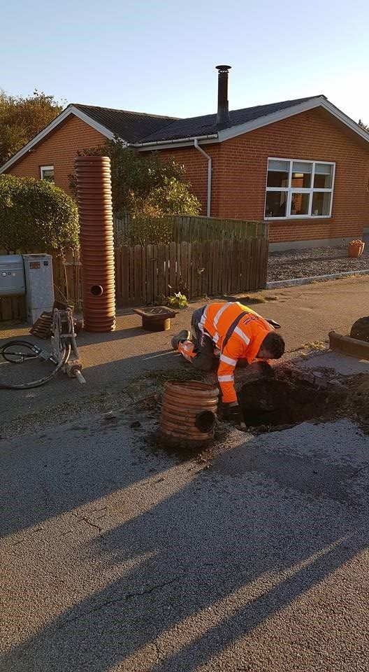 En mand er ved at grave et hul i jorden foran et hus.