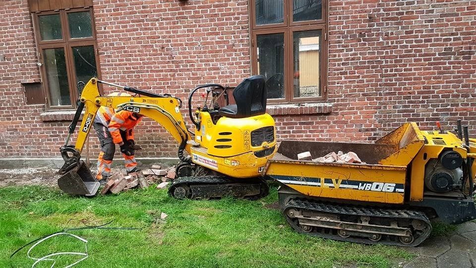 En mand arbejder på en lille gravemaskine ved siden af en dumper.