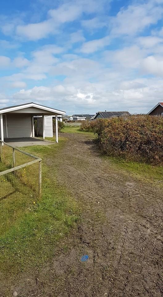 En grusvej, der fører til et hus midt på en mark.