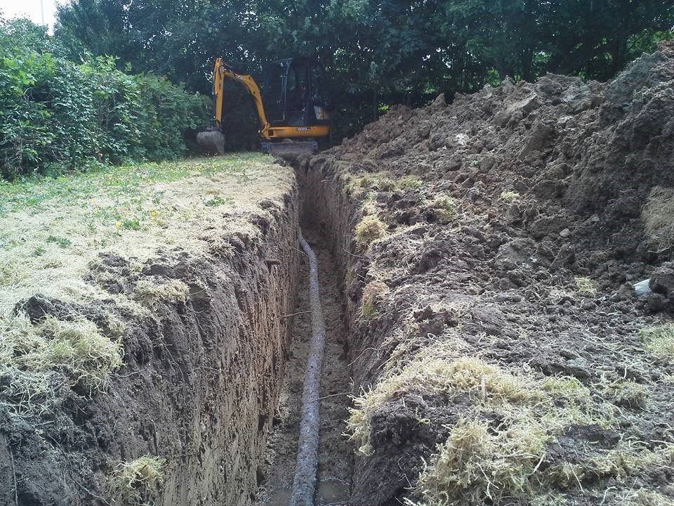 En gul gravemaskine graver en rende i jorden