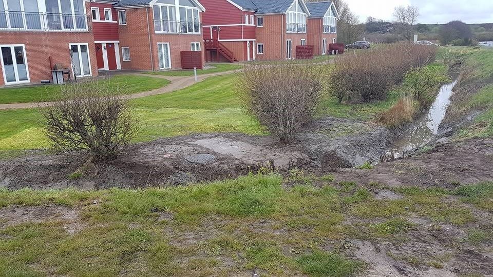 Der løber et vandløb gennem græsset foran en murstensbygning.