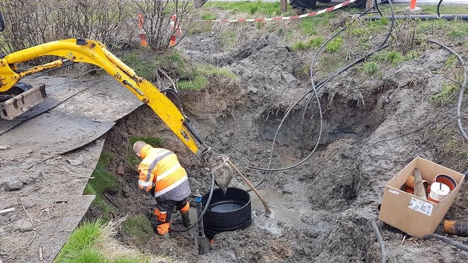 En mand knæler i mudderet ved siden af ​​en gul gravemaskine.