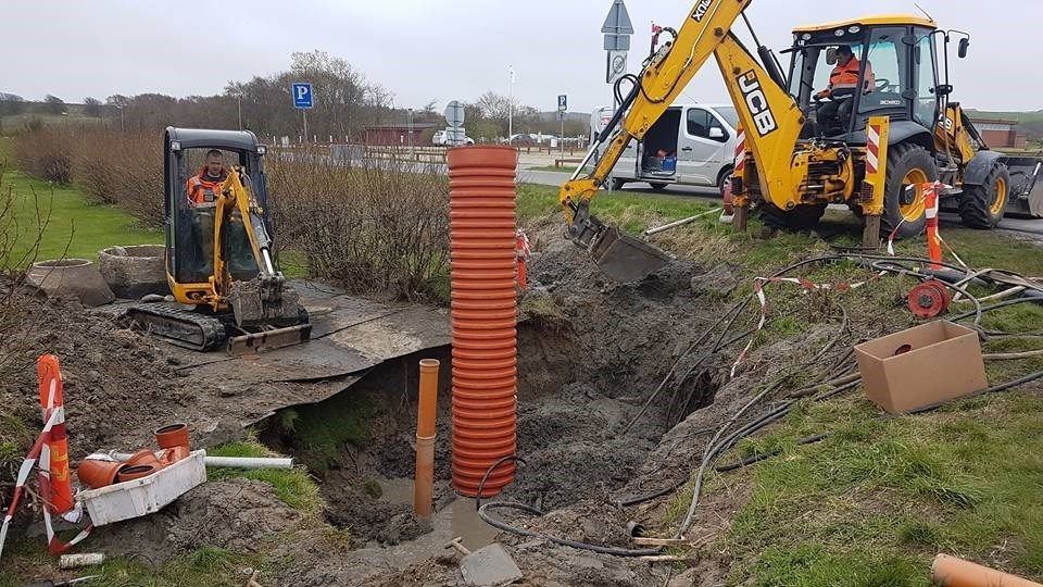 En gul gravemaskine er ved at grave et hul i jorden.