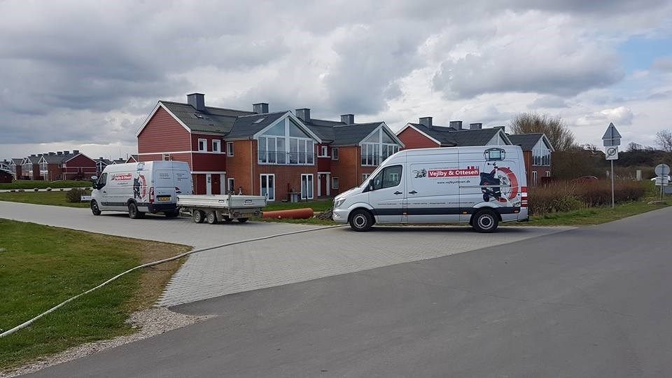 To varebiler er parkeret i vejkanten foran en række huse.