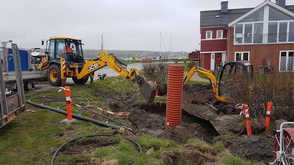 En traktor graver et hul i jorden foran et hus.