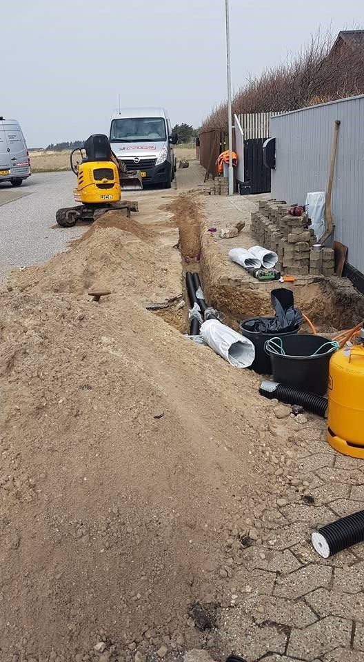 En gul gravemaskine er ved at grave et hul i siden af ​​en vej.