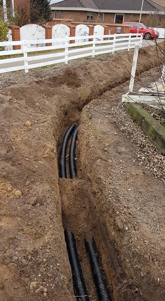 En flok sorte rør ligger i jorden ved siden af ​​et hvidt hegn.