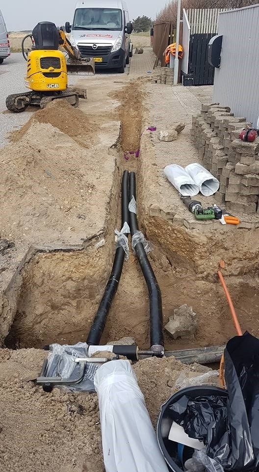 En gul gravemaskine graver en rende i jorden ved siden af ​​en varevogn.