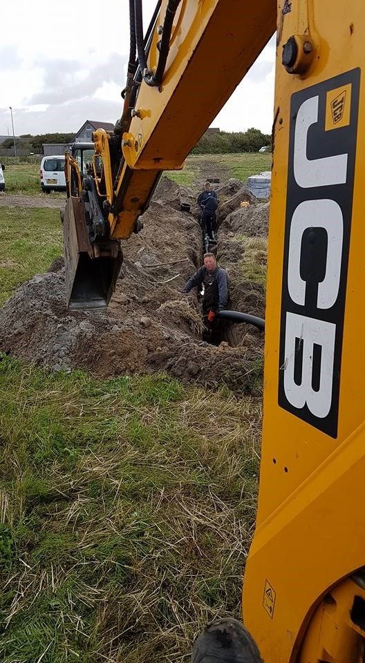 En gul jcb gravemaskine graver et hul på en mark.