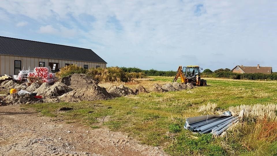 En traktor graver et hul på en mark foran en bygning.