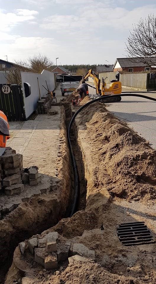 En mand graver et hul i jorden for at installere et rør.