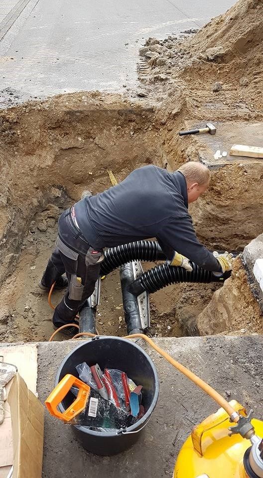 En mand arbejder på et rør i jorden ved siden af en spand værktøj.