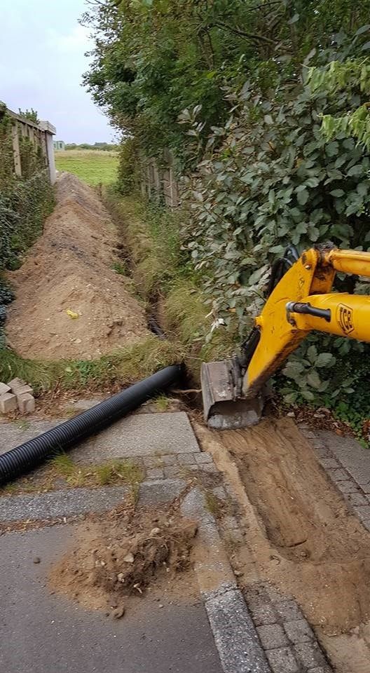 En gul gravemaskine graver et hul i jorden ved siden af en vej.