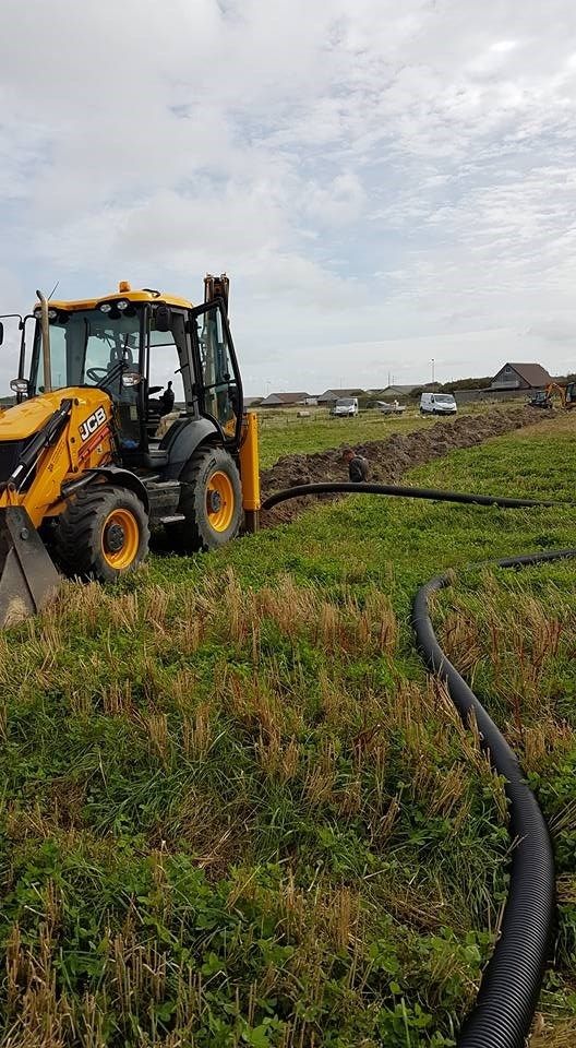 En gul traktor kører gennem en græsmark med en slange fastgjort til den.