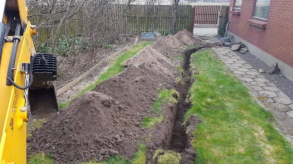 En gul gravemaskine graver en rende i en gård.