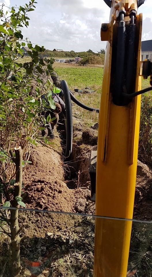 En gul gravemaskine graver et hul i jorden på en mark.