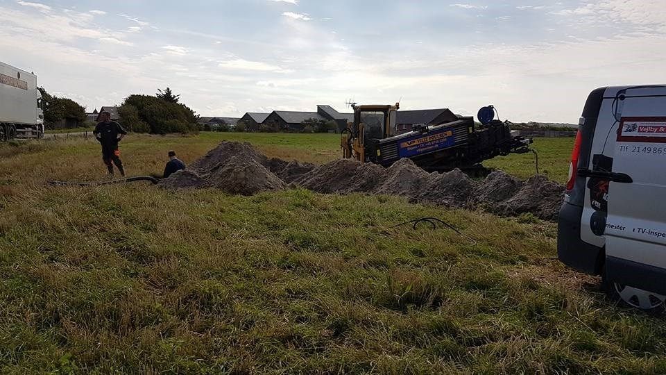 En traktor graver et hul på en mark ved siden af en varevogn.